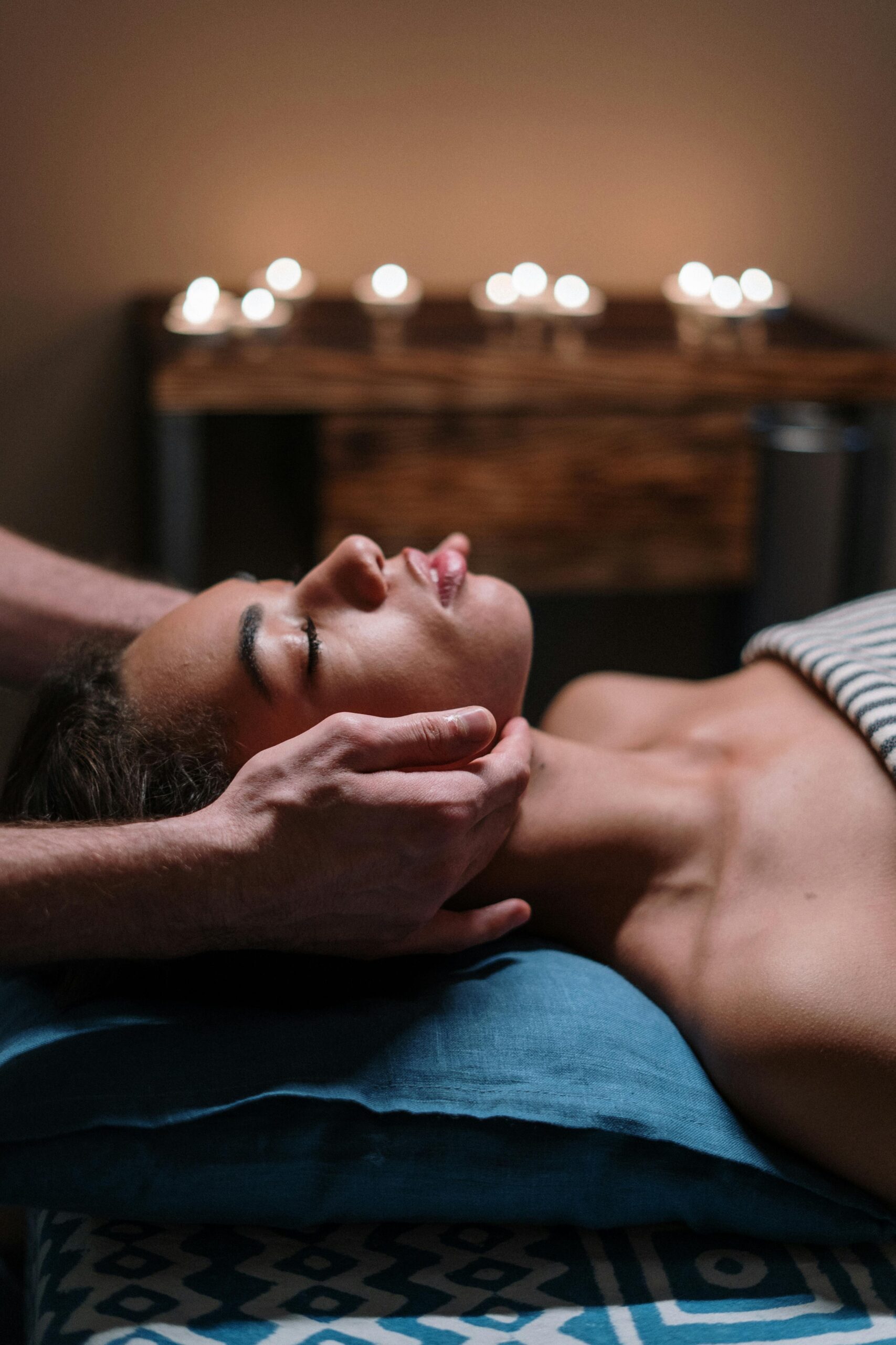 Natural Lift Facial Massage in Moray Woman receiving a calming facial massage in a tranquil spa setting with candlelight.